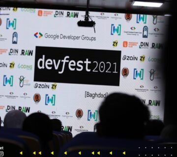 Stage backdrop displays devfest 2021 banner with Google Developer Groups logos; audience silhouettes in foreground 