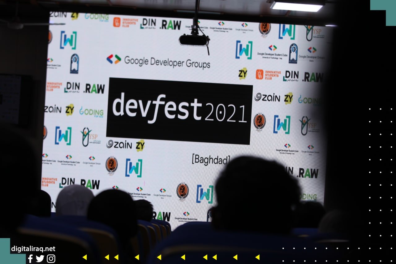 Stage backdrop displays devfest 2021 banner with Google Developer Groups logos; audience silhouettes in foreground 